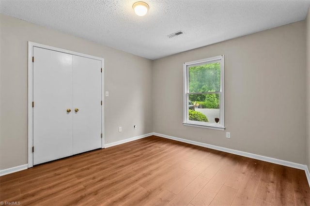 unfurnished bedroom with wood finished floors, visible vents, a textured ceiling, and baseboards
