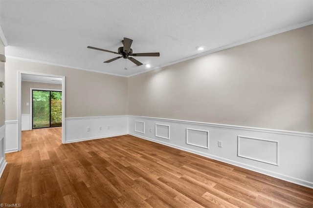 empty room with wainscoting, ornamental molding, a ceiling fan, and wood finished floors