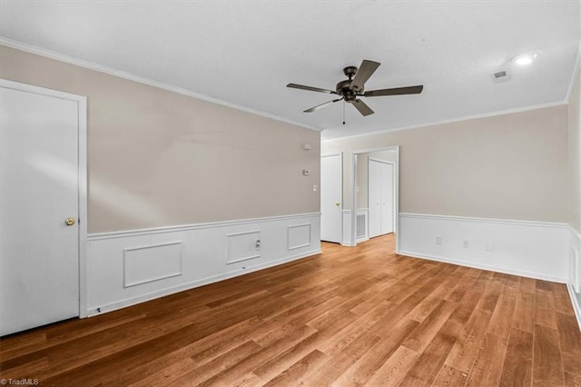 empty room with ornamental molding, a wainscoted wall, ceiling fan, and light wood-type flooring