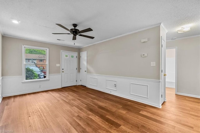 unfurnished room with wood finished floors, wainscoting, ornamental molding, ceiling fan, and a textured ceiling