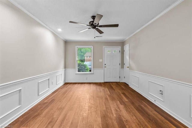 interior space with crown molding, a ceiling fan, wainscoting, and wood finished floors