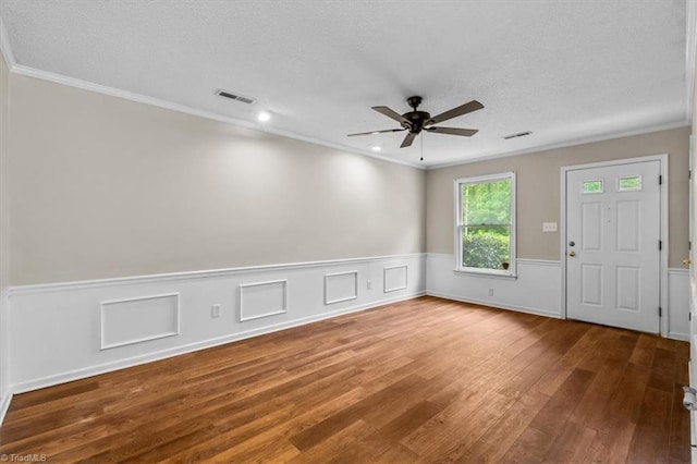 unfurnished room with ceiling fan, ornamental molding, a textured ceiling, wainscoting, and wood finished floors