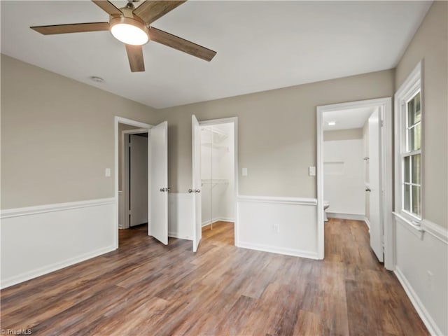 unfurnished bedroom featuring baseboards, ceiling fan, wood finished floors, a spacious closet, and a closet