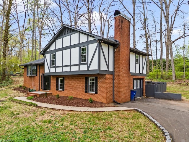 view of side of property with driveway, brick siding, a chimney, a yard, and stucco siding