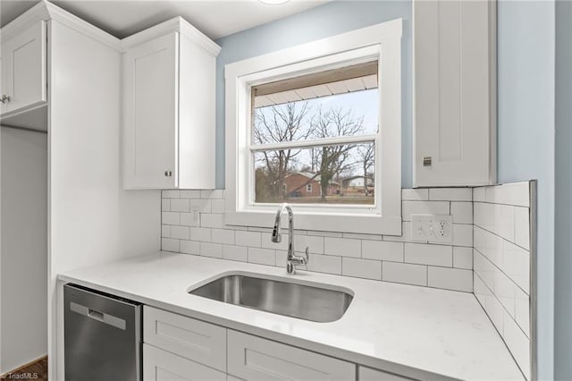 kitchen with decorative backsplash, white cabinetry, sink, and stainless steel dishwasher