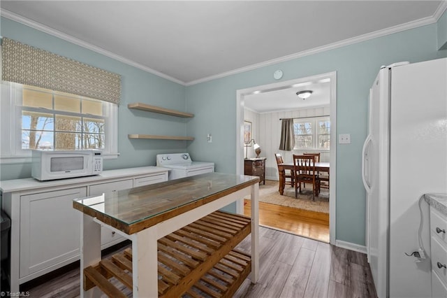 kitchen featuring wood-type flooring, ornamental molding, white appliances, washing machine and dryer, and white cabinets