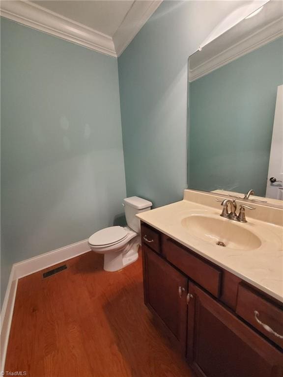 half bathroom with visible vents, toilet, wood finished floors, crown molding, and vanity