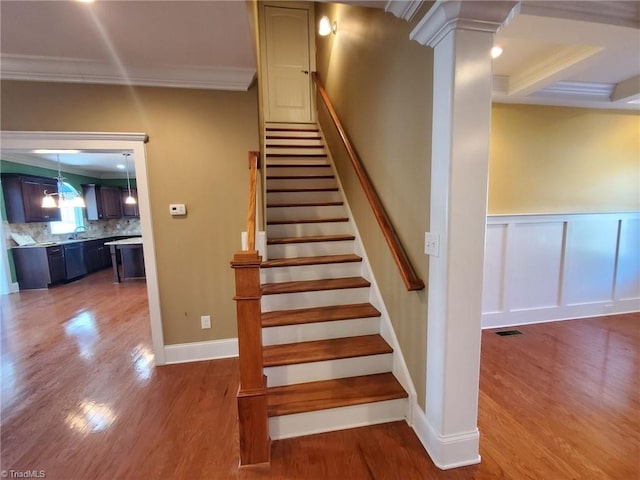 stairway featuring wood finished floors, visible vents, ornamental molding, wainscoting, and ornate columns