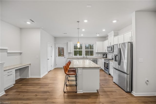 kitchen with light stone countertops, appliances with stainless steel finishes, decorative light fixtures, a kitchen island, and white cabinetry