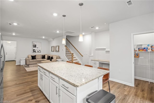 kitchen featuring white cabinetry, light stone countertops, decorative light fixtures, a kitchen island, and light wood-type flooring