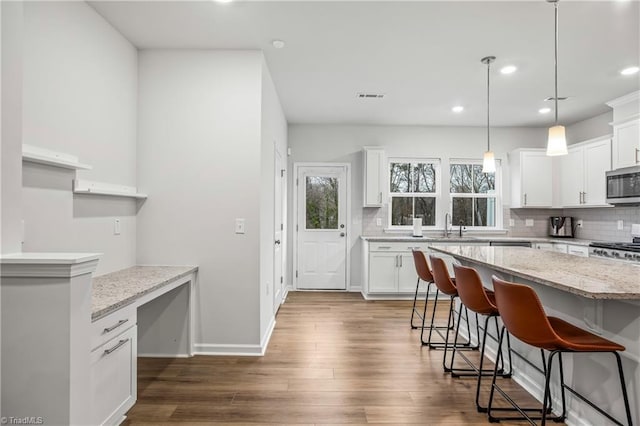 kitchen with a kitchen bar, backsplash, light stone counters, pendant lighting, and white cabinetry