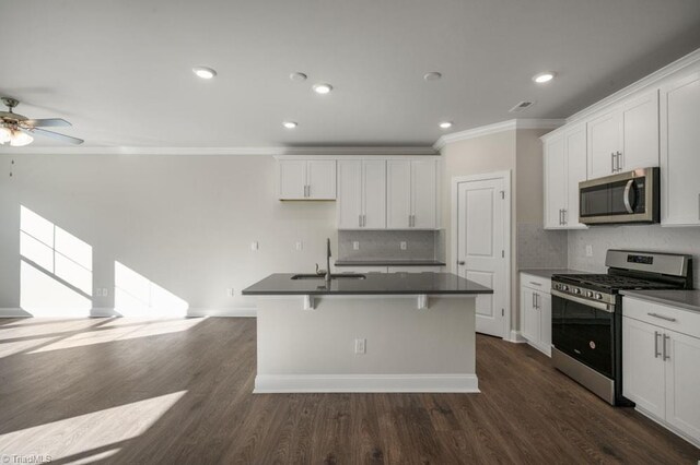 1404 Amberview Ln, Kernersville, NC 27284 - kitchen featuring a kitchen island with sink, a sink, dark countertops, appliances with stainless steel finishes, and ornamental molding