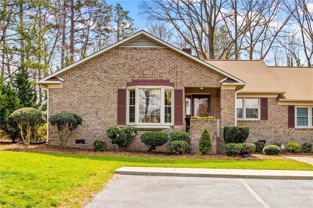 view of front of home featuring brick siding, uncovered parking, a front lawn, and crawl space