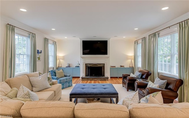 living room with recessed lighting, ornamental molding, a fireplace with raised hearth, and light wood-type flooring