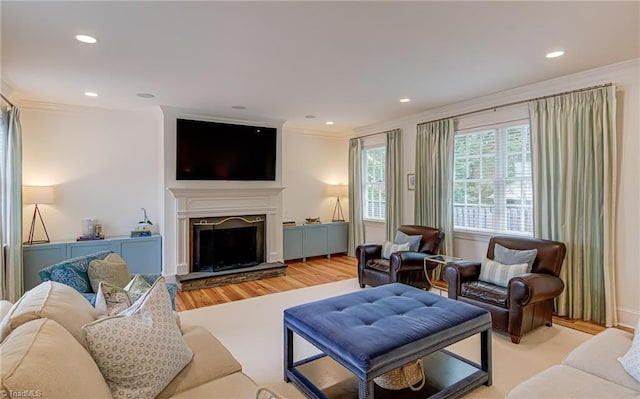 living room with recessed lighting, ornamental molding, a fireplace with raised hearth, and wood finished floors