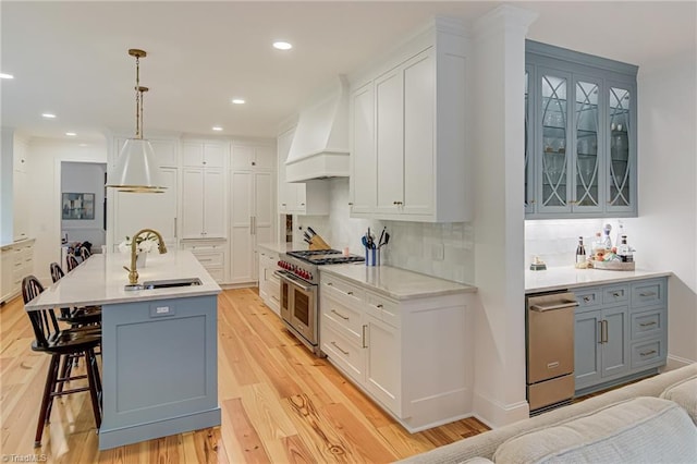 kitchen featuring appliances with stainless steel finishes, a sink, gray cabinets, premium range hood, and a kitchen bar