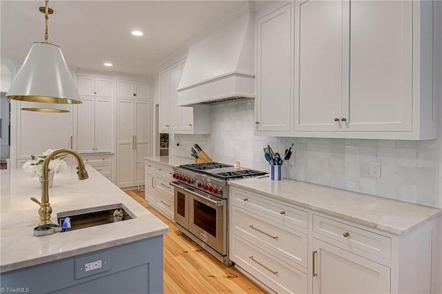 kitchen featuring white cabinets, a sink, premium range hood, range with two ovens, and decorative backsplash
