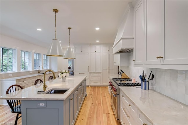 kitchen featuring a kitchen breakfast bar, a sink, stainless steel range, light wood finished floors, and white cabinetry