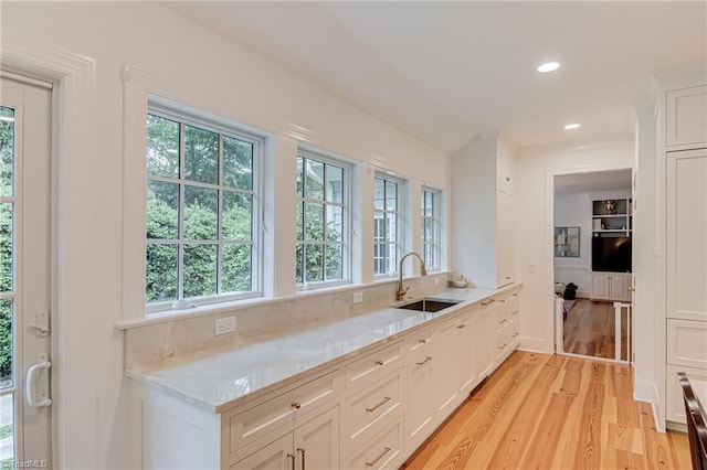 kitchen featuring light stone countertops, a sink, white cabinets, light wood-style floors, and recessed lighting