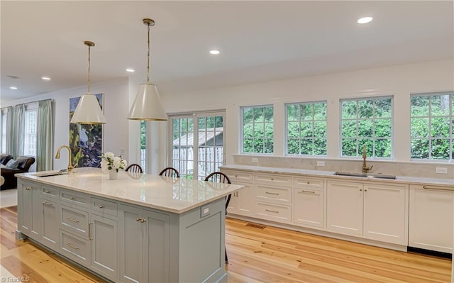kitchen with a sink, a kitchen island with sink, gray cabinetry, and light wood-type flooring