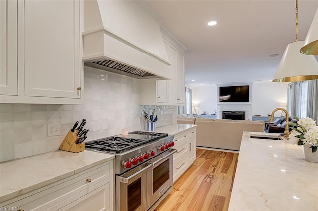 kitchen featuring double oven range, a sink, white cabinets, custom exhaust hood, and light wood-style flooring