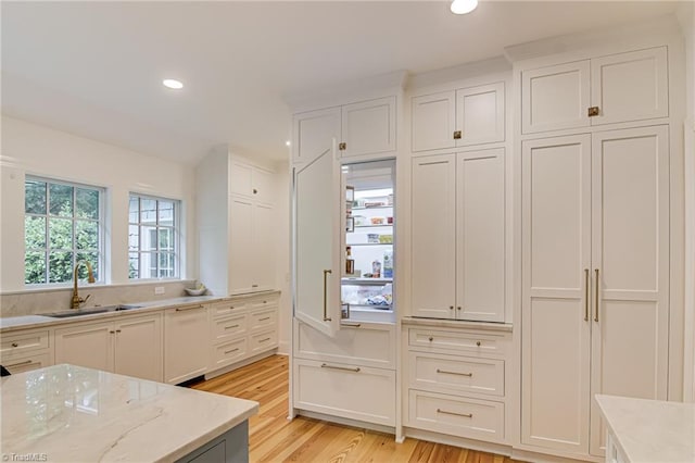 kitchen with a sink, light stone counters, white cabinets, light wood finished floors, and recessed lighting