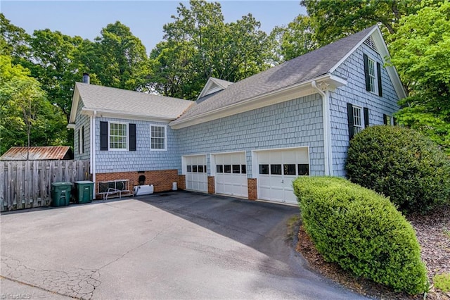 view of side of home featuring a garage, fence, a chimney, a shingled roof, and driveway