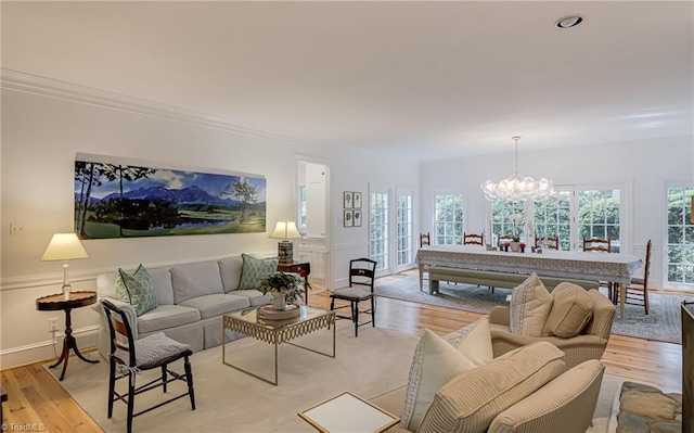 living room with baseboards, a chandelier, ornamental molding, and light wood-style floors