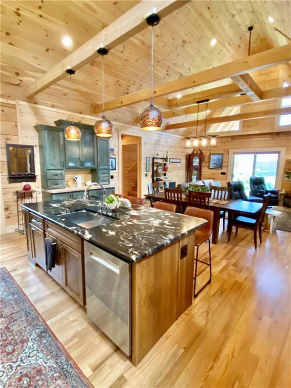 1295 Will Vannoy Rd, West Jefferson, NC 28694 - kitchen featuring stainless steel dishwasher, wood walls, light wood finished floors, wood ceiling, and a center island with sink