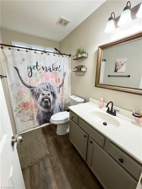 bathroom featuring curtained shower, toilet, wood finished floors, vanity, and visible vents