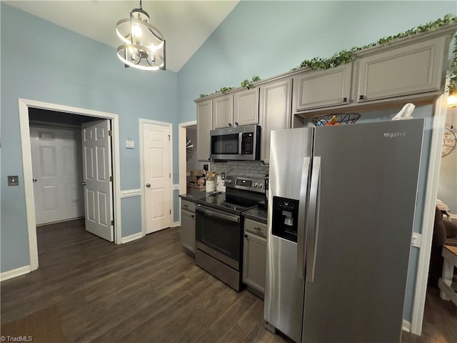 kitchen with appliances with stainless steel finishes, dark wood-style floors, tasteful backsplash, dark countertops, and an inviting chandelier