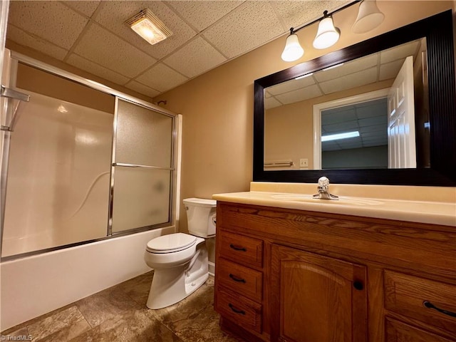 full bathroom featuring a drop ceiling, enclosed tub / shower combo, vanity, and toilet