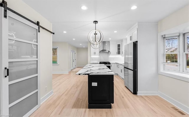 kitchen featuring white cabinets, a center island, wall chimney exhaust hood, stainless steel fridge, and pendant lighting