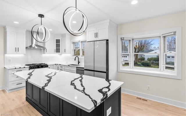 kitchen with stainless steel appliances, white cabinetry, light hardwood / wood-style floors, hanging light fixtures, and a kitchen island