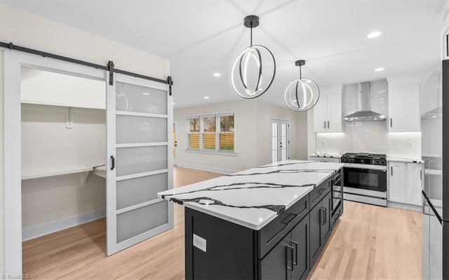 kitchen featuring white cabinets, wall chimney range hood, decorative light fixtures, and gas range oven