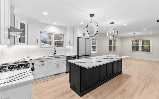 kitchen featuring stainless steel appliances, sink, white cabinetry, a center island, and hanging light fixtures