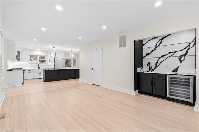 unfurnished living room featuring indoor bar, beverage cooler, and light hardwood / wood-style flooring