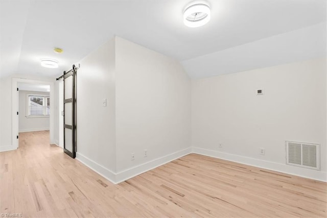 additional living space featuring light hardwood / wood-style floors, vaulted ceiling, and a barn door