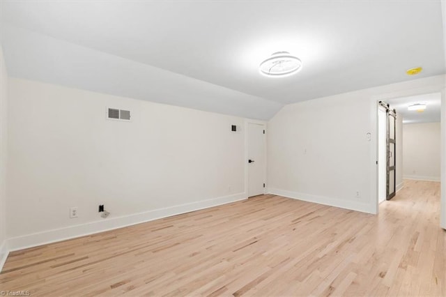 spare room featuring vaulted ceiling, light hardwood / wood-style floors, and a barn door