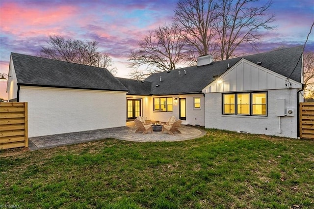 back house at dusk featuring a patio and a lawn