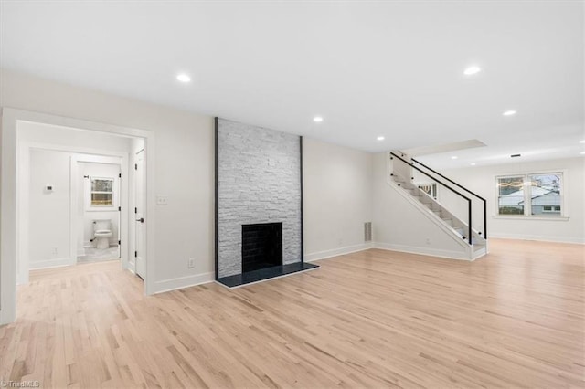 unfurnished living room with light wood-type flooring and a stone fireplace