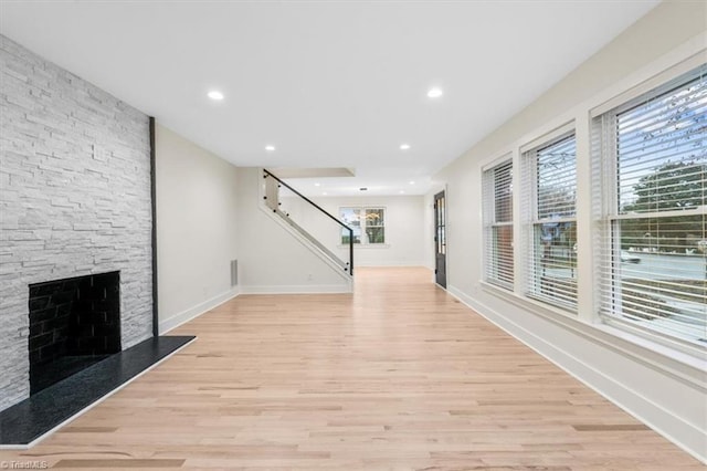 unfurnished living room featuring a wealth of natural light, light hardwood / wood-style flooring, and a stone fireplace