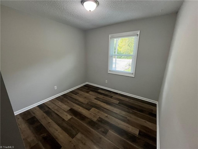 spare room with a textured ceiling and dark hardwood / wood-style flooring