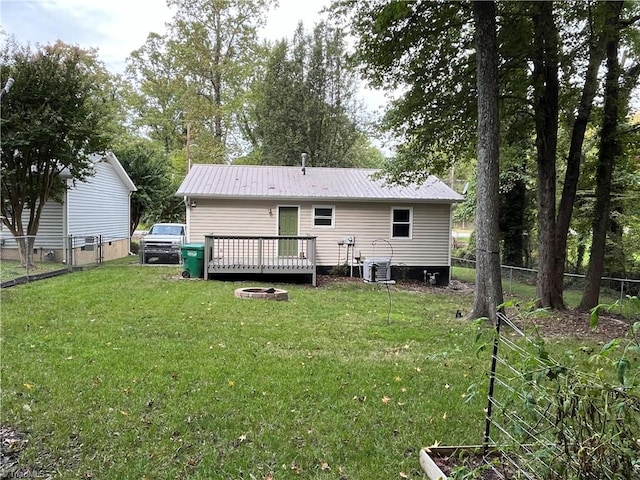 rear view of house featuring cooling unit, a wooden deck, a lawn, and an outdoor fire pit