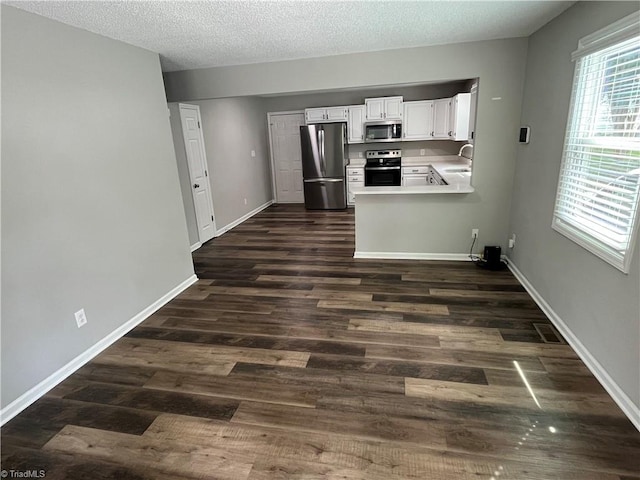 kitchen featuring kitchen peninsula, white cabinetry, dark wood-type flooring, and stainless steel appliances