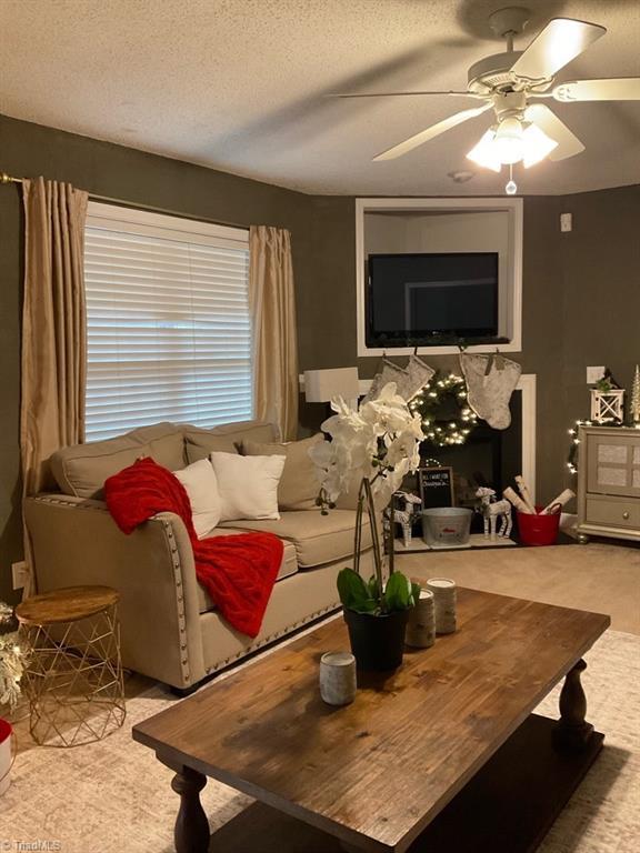 carpeted living room with ceiling fan and a textured ceiling