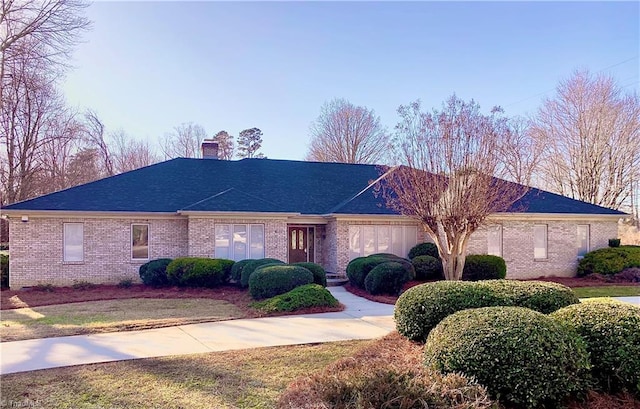 ranch-style house featuring roof with shingles, a chimney, and brick siding