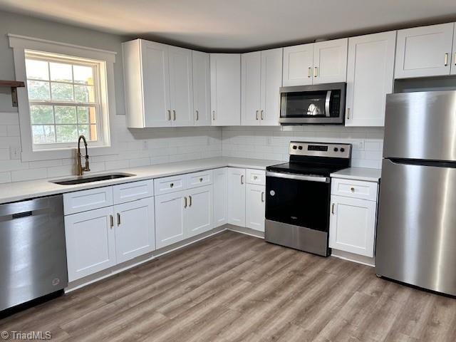 kitchen featuring stainless steel appliances, light countertops, light wood-style floors, white cabinets, and a sink