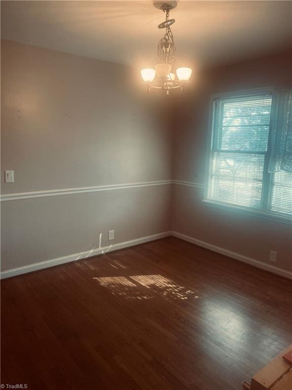 spare room with a chandelier and dark wood-type flooring