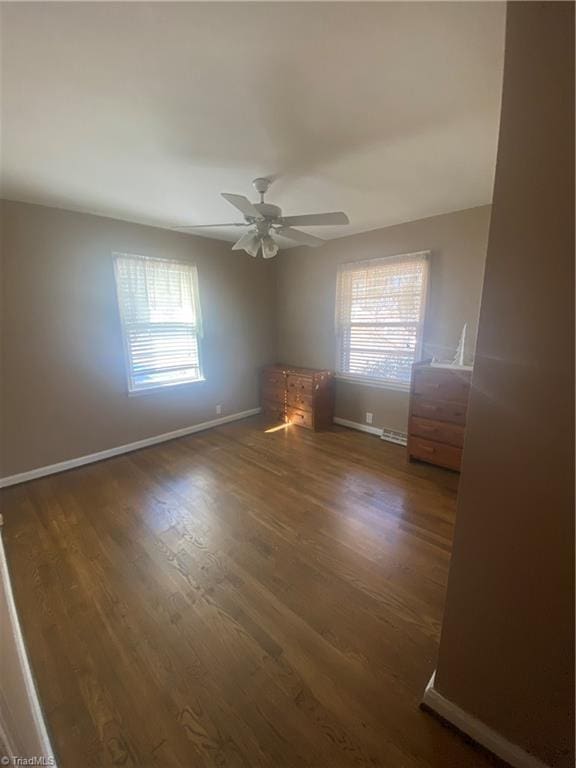 empty room featuring ceiling fan, a healthy amount of sunlight, and dark hardwood / wood-style floors